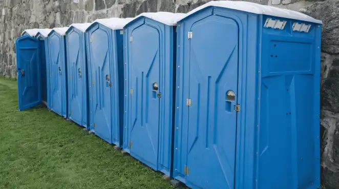 Row of blue portable toilets lined up on grass against a stone wall for event sanitation in Detroit, MI