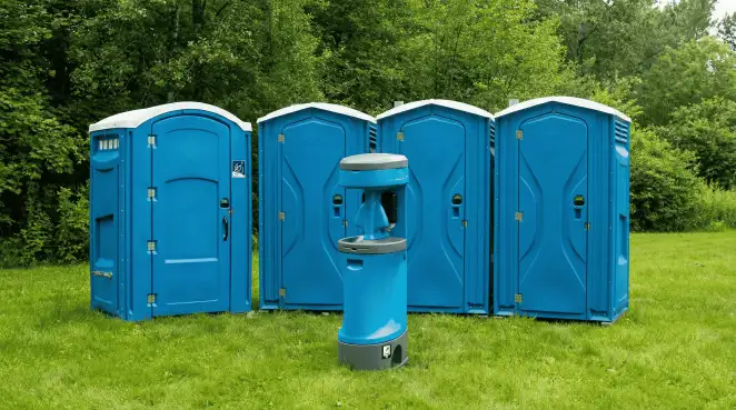 Four blue portable toilets and a matching hand washing station on grass near trees, a common sight at local outdoor events in Detroit, MI