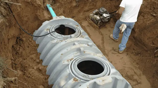 Septic tank installation showing a technician compacting soil around a new poly septic tank in an excavation pit in Detroit, MI